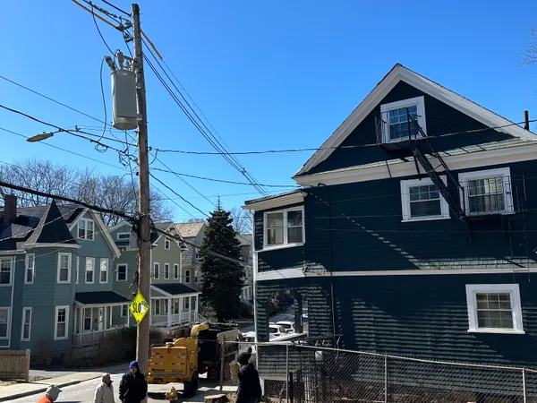 Four of the crew in the street beside a loaded dump truck, working a removal in front of a green three-decker on a dense residential block.